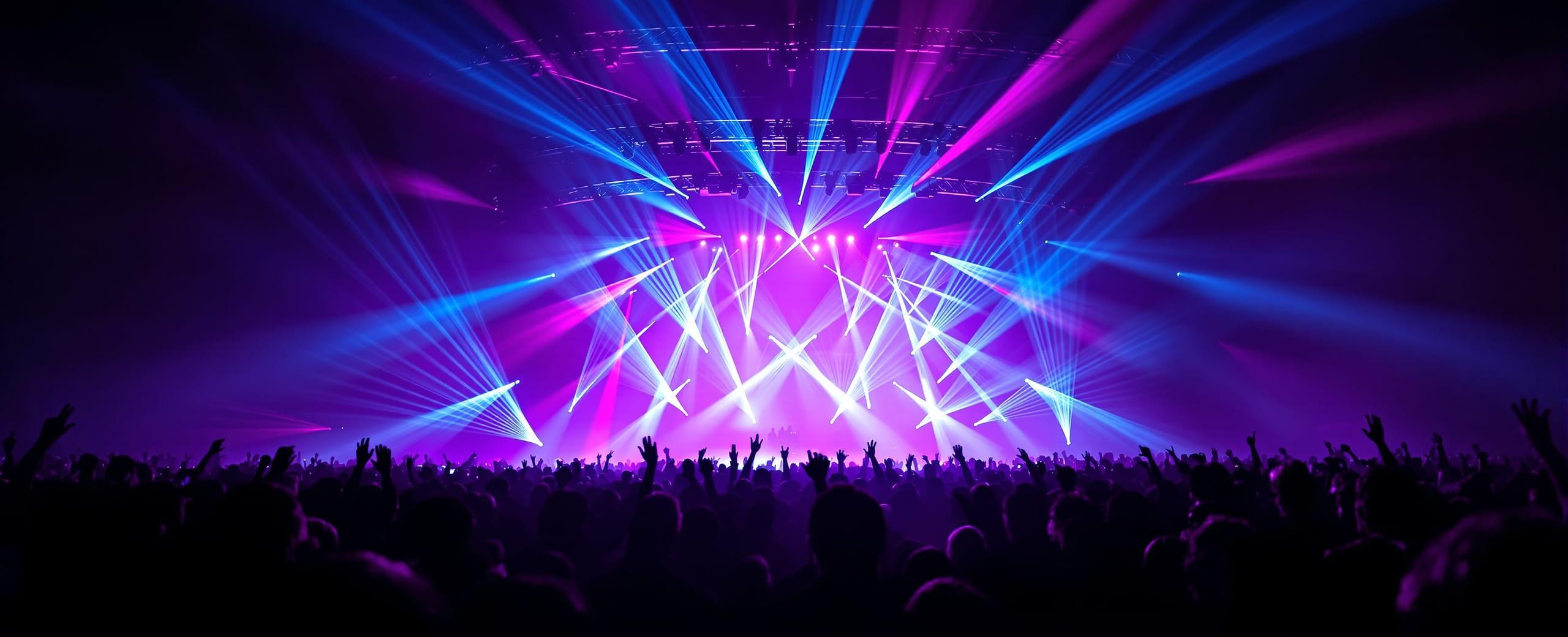 Show de iluminación profesional con haces de luz violeta, azul y magenta sobre el público de un evento