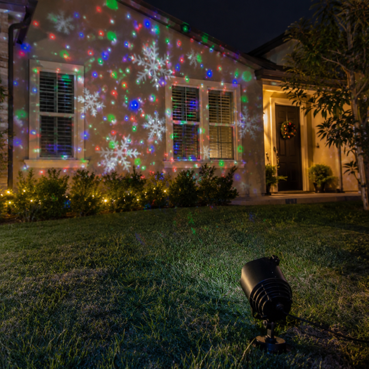 Proyector LED navideño iluminando la fachada de una casa desde el suelo